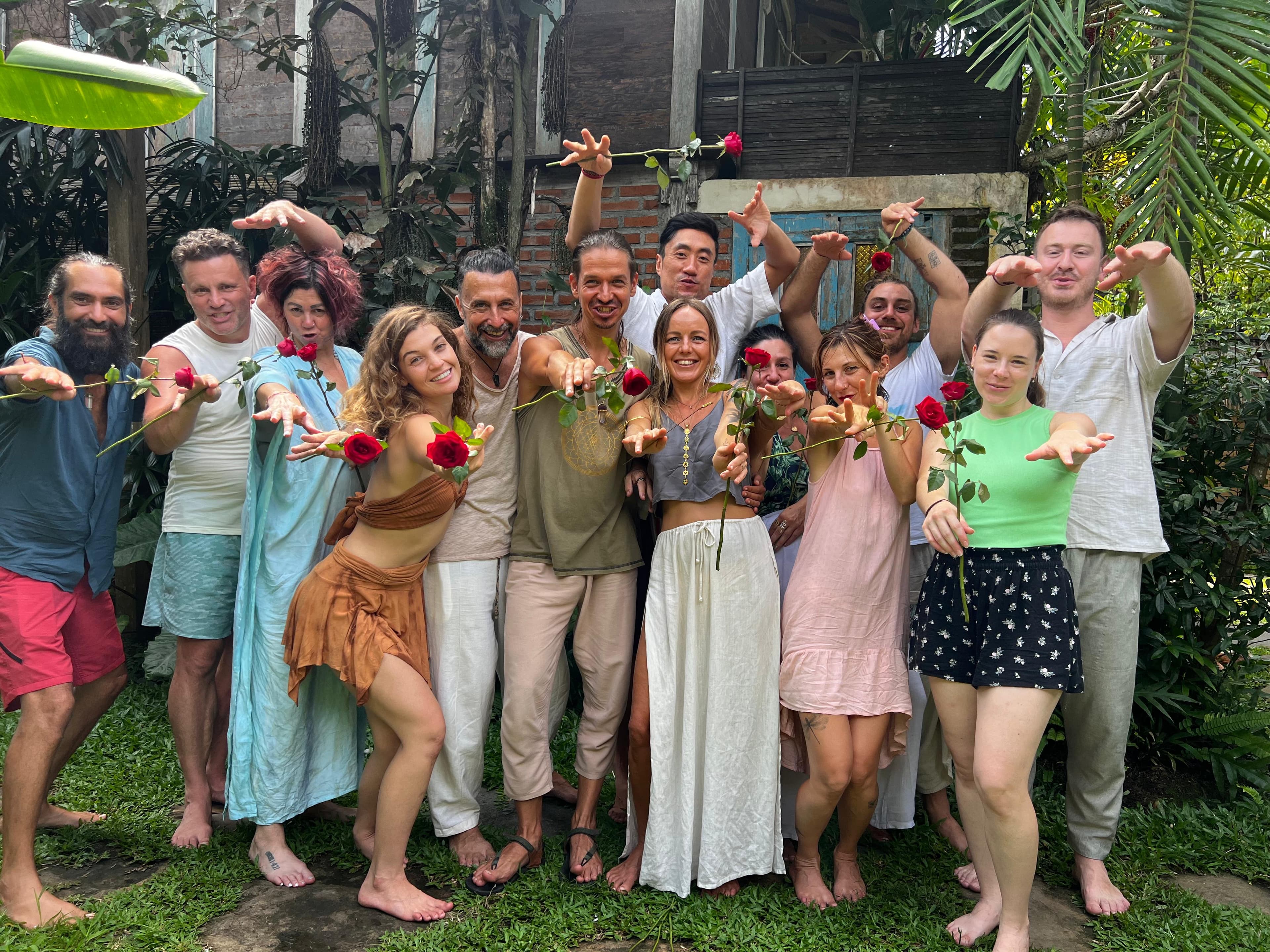 Retreat participants gathered in a Bali garden, smiling and reaching toward the camera with red roses in hand